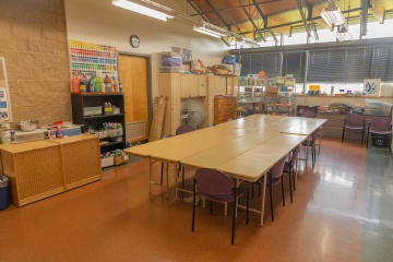 small room with long rectangular table in the center surrounded by a wall of shelves with crafting materials